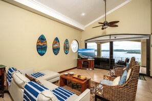 A living room with a sofa, a television, and a view of the sea.