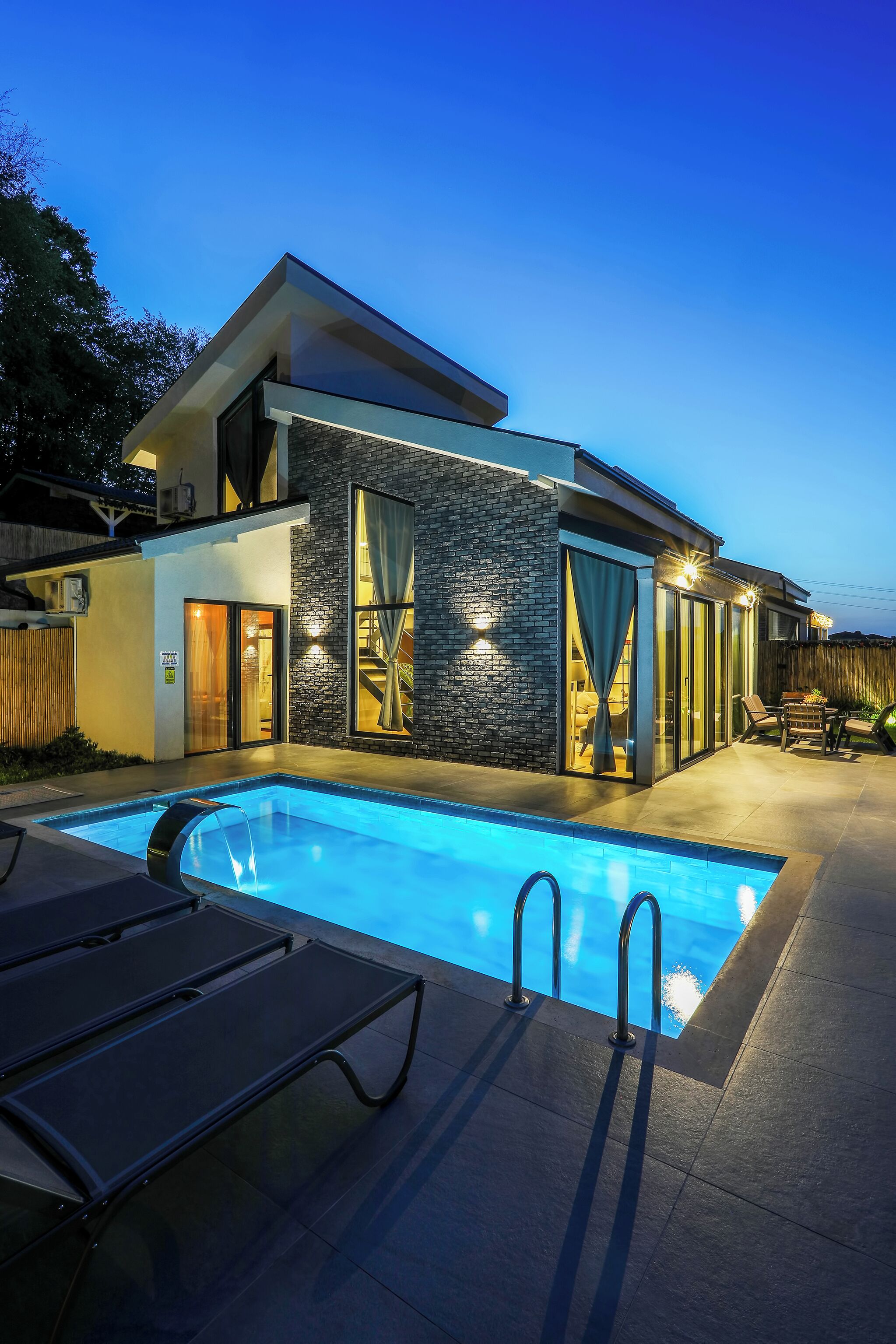A modern house with a swimming pool, outdoor seating, and a staircase leading to the upper level.
