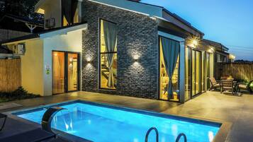 A modern house with a swimming pool, outdoor seating, and a staircase leading to the upper level.