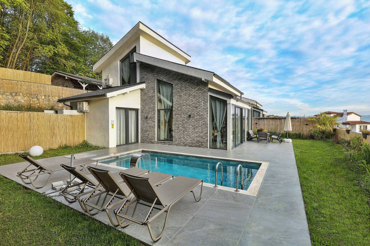 Ein modernes Haus mit Schwimmbad, Sitzgelegenheiten im Freien und einem Holzzaun.
