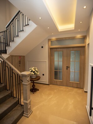 Un intérieur moderne avec un escalier, une porte en bois dotée de panneaux en verre dépoli et une table ronde agrémentée d’un arrangement floral.