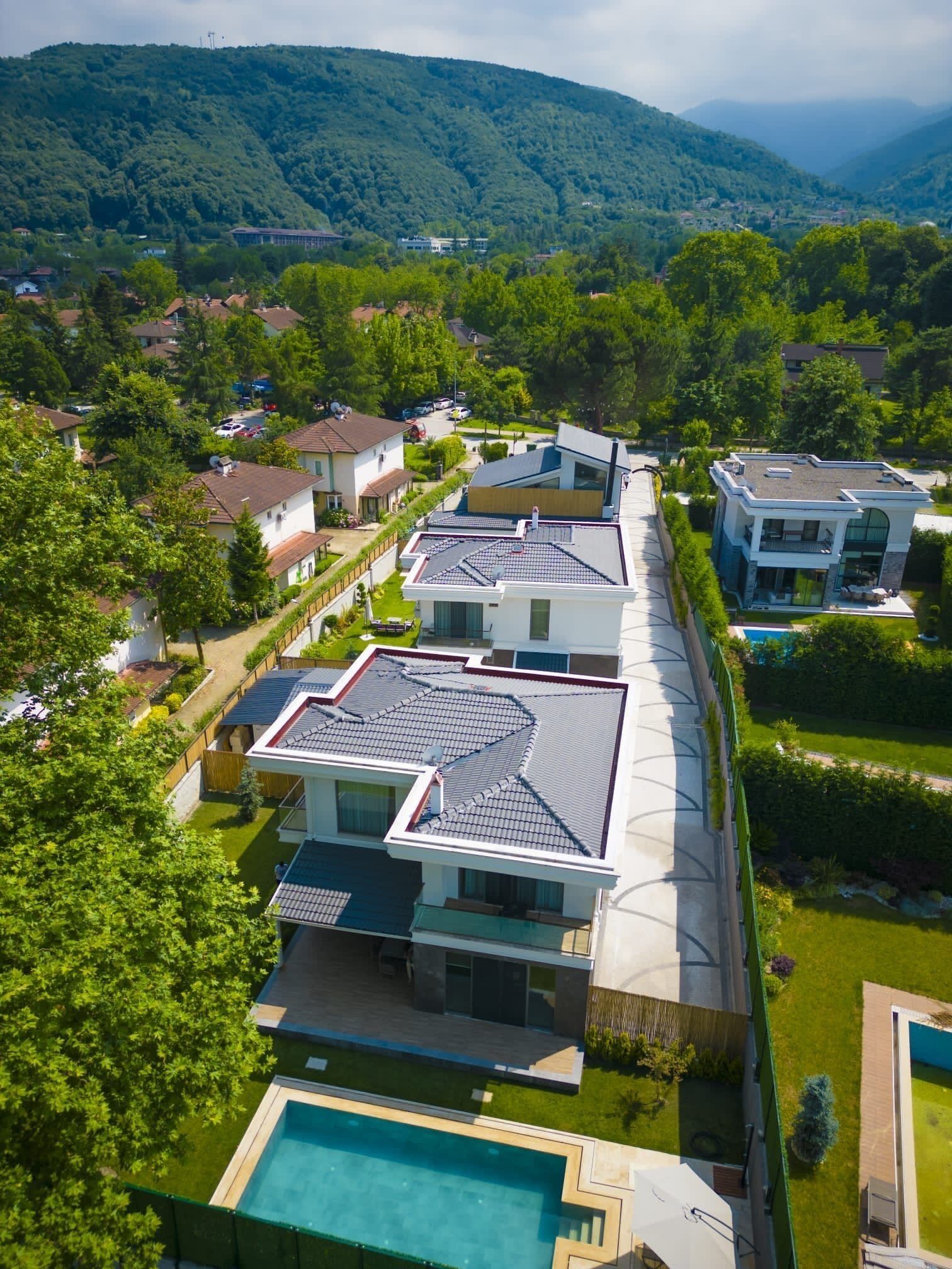 Un moderno complejo residencial con varias casas, una piscina y un paisaje montañoso de fondo.