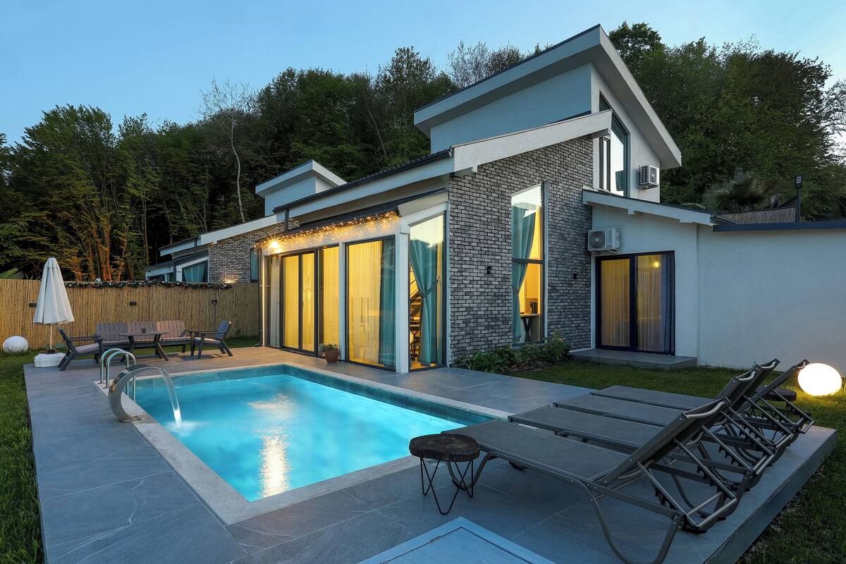 Ein modernes Haus mit Schwimmbad, Sitzgelegenheiten im Freien und einem gepflegten Garten.