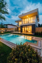 A modern two-story house with a swimming pool, a covered patio, and a well-maintained lawn.