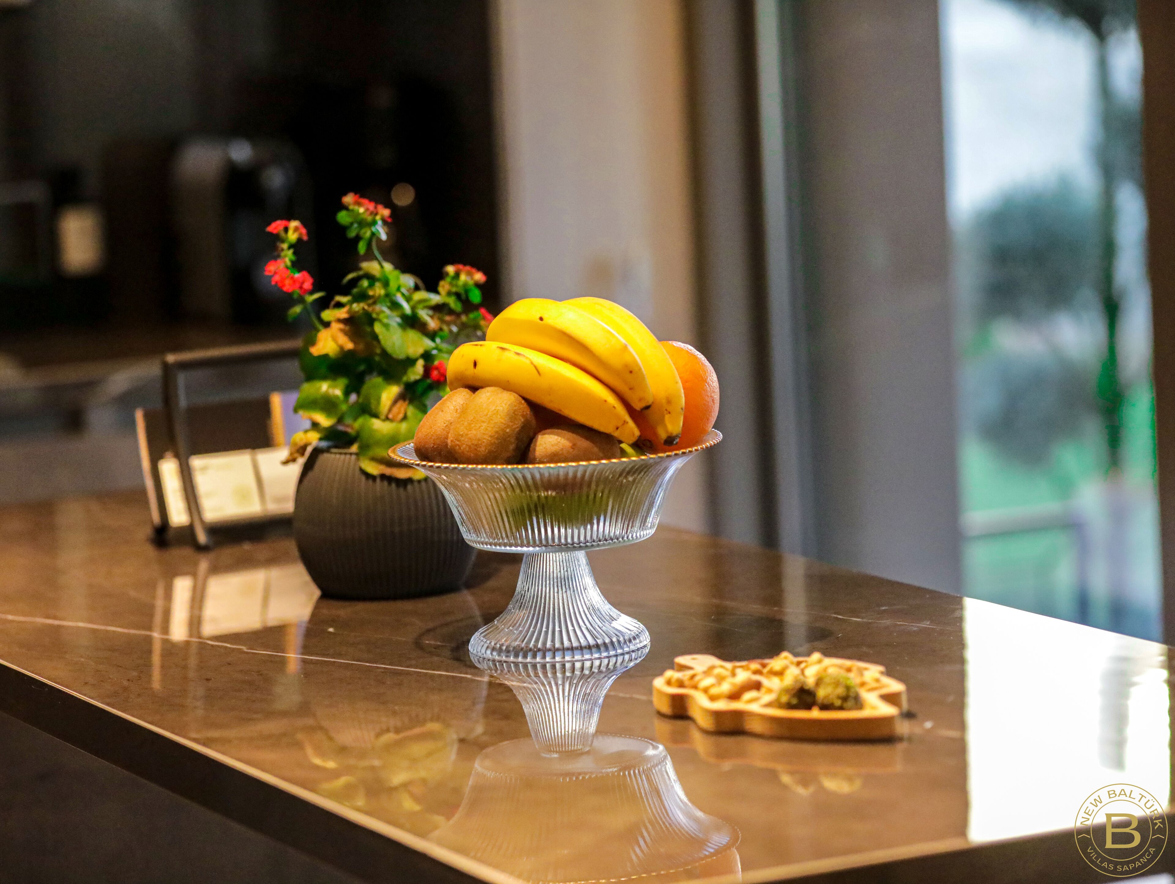 Une table avec un panier de fruits contenant des bananes et des oranges, un vase avec des fleurs et une assiette de gaufres.