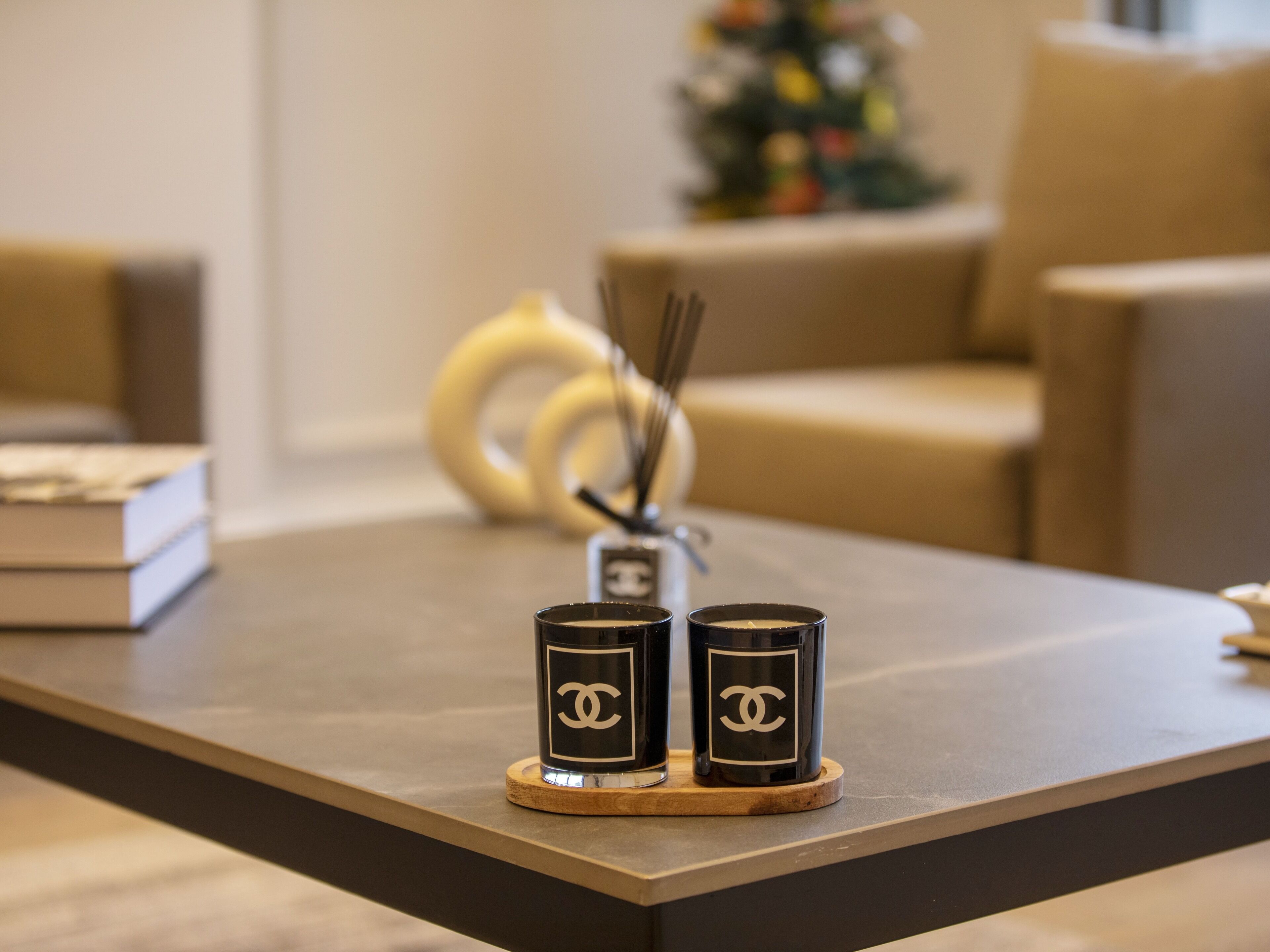 A table with two black candle holders with a white logo, a wooden coaster, and a pair of black candles.