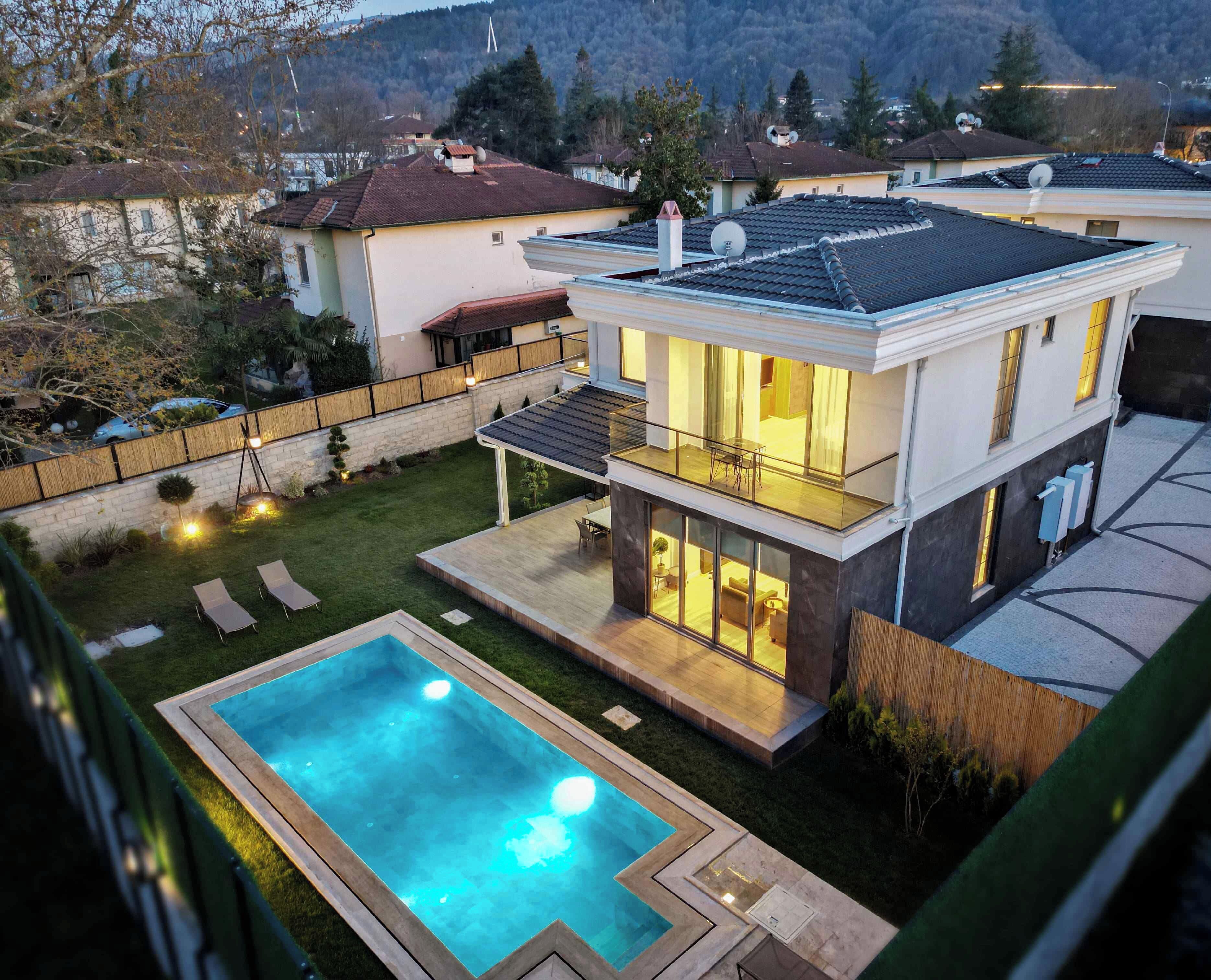 A modern two-story house with a swimming pool, a balcony, and a well-maintained garden.