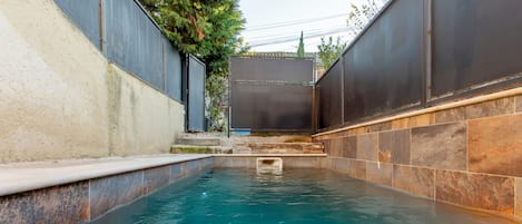A swimming pool with a tiled edge, surrounded by walls with a mix of stone and metal panels.