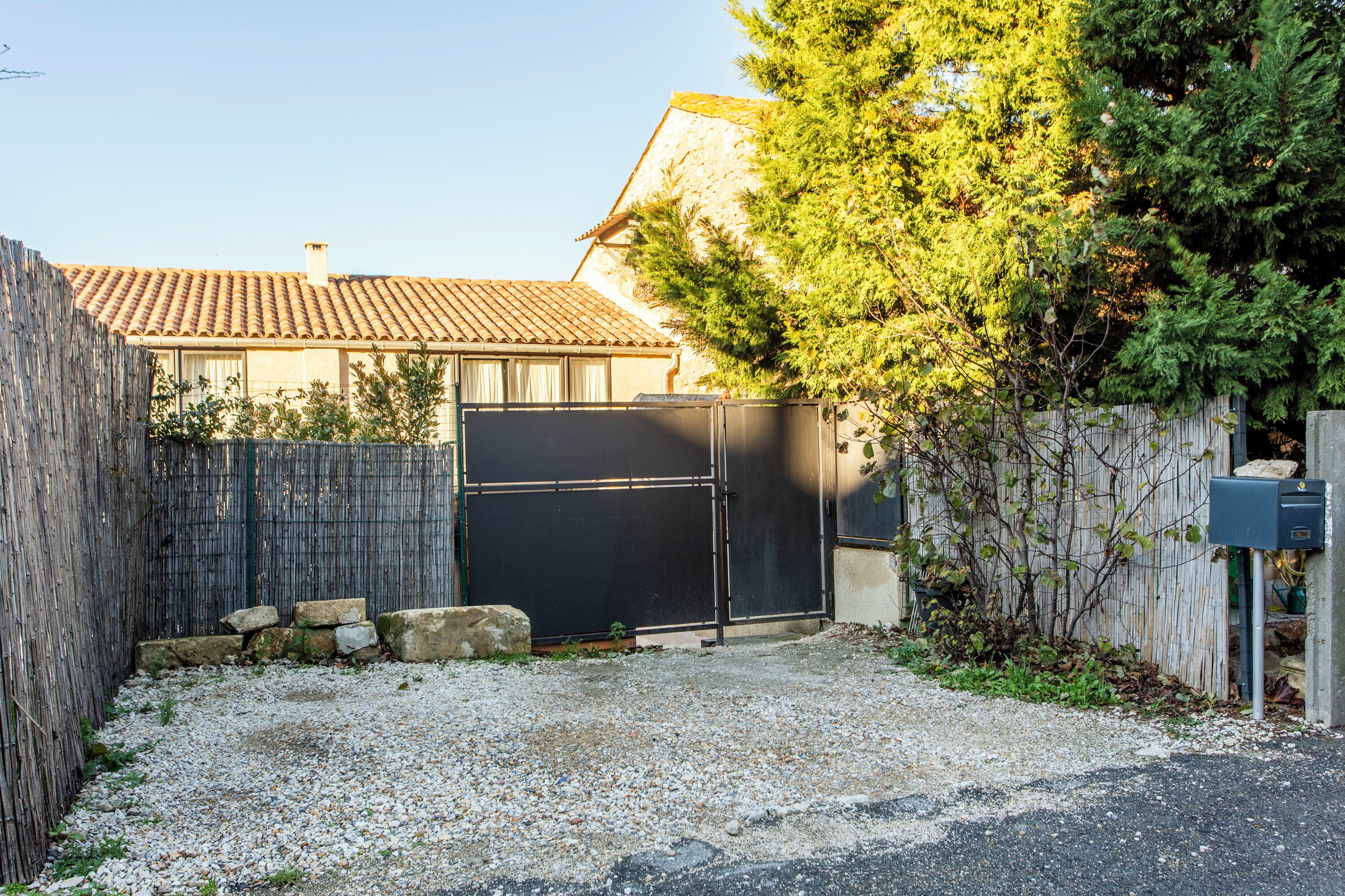 Una propietat residencial amb un camí d'accés tancat per una porta, un camí de grava i una casa amb teulada de rajola.