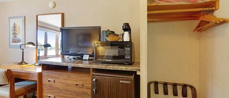 A compact hotel room with a kitchenette, a desk with a computer, a chair, a microwave, and a small refrigerator.