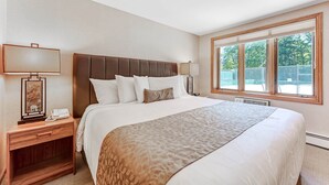 A hotel room with a large bed, a nightstand with a lamp, and a window with a view of trees. - Chanticleer Inn 37 (Washington)