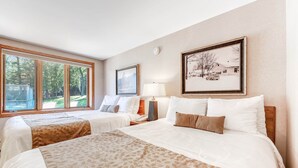 Une chambre d’hôtel avec deux lits, une grande fenêtre, une lampe et des tableaux encadrés au mur.