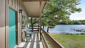 Une véranda donnant sur un lac, avec des chaises vertes et une porte.