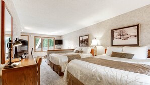 Een hotelkamer met twee bedden, een bureau, een televisie en een raam met uitzicht op bomen.