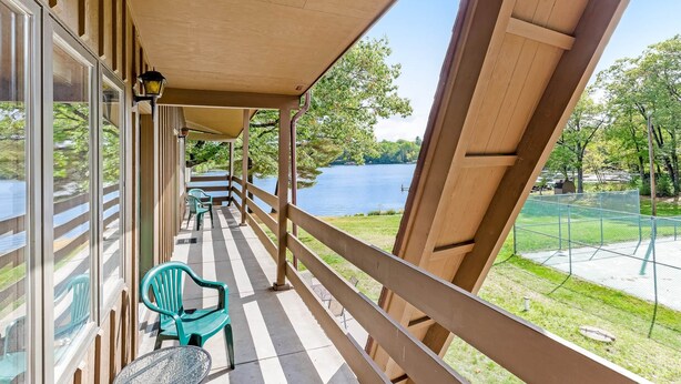 Een overdekt balkon met uitzicht op een meer, houten leuningen en groene stoelen.