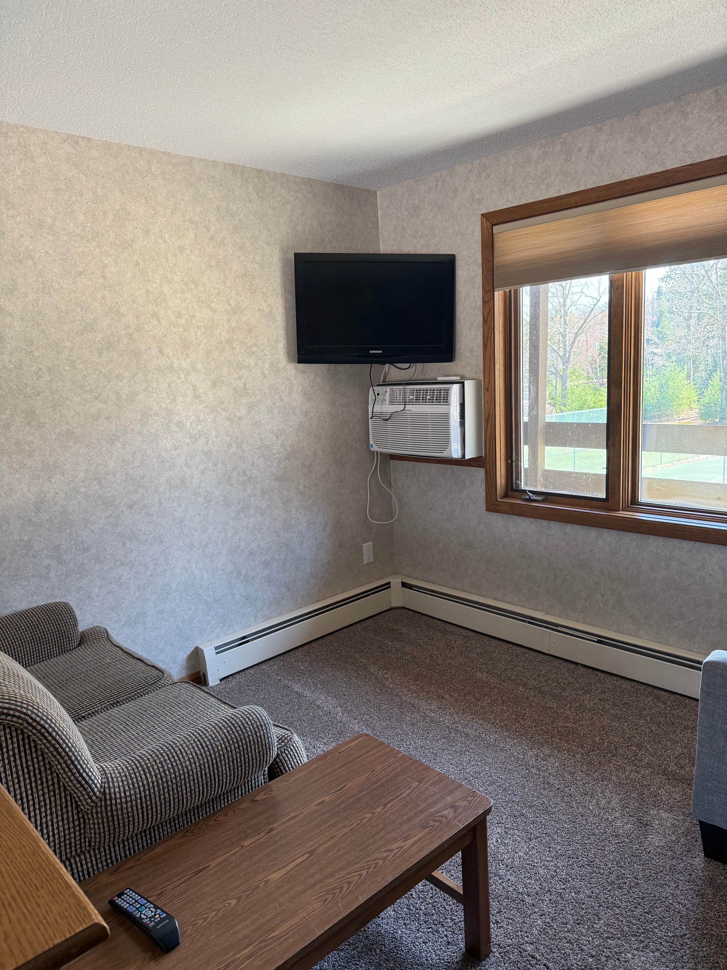 A living room with a flat-screen TV mounted on the wall, a built-in air conditioning unit, a wooden coffee table, and a couch.