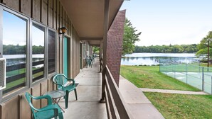 A covered outdoor area with a view of a lake, green chairs, and a pathway leading to a fenced sports area. - Chanticleer Inn 44 (Eagle River)