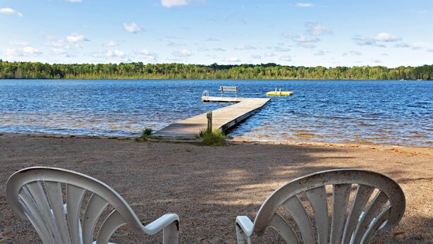 A lakeside view with a dock extending into the water, surrounded by chairs and a bench. - Chanticleer Inn 44 (Eagle River)