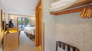 Una habitación de hotel con un escritorio de madera, una cama con edredón blanco, un balcón con vistas y un perchero con toallas.