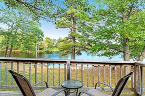 A wooden deck with a glass table and chairs overlooking a lake and trees. - Chanticleer Inn 52 (Eagle River)