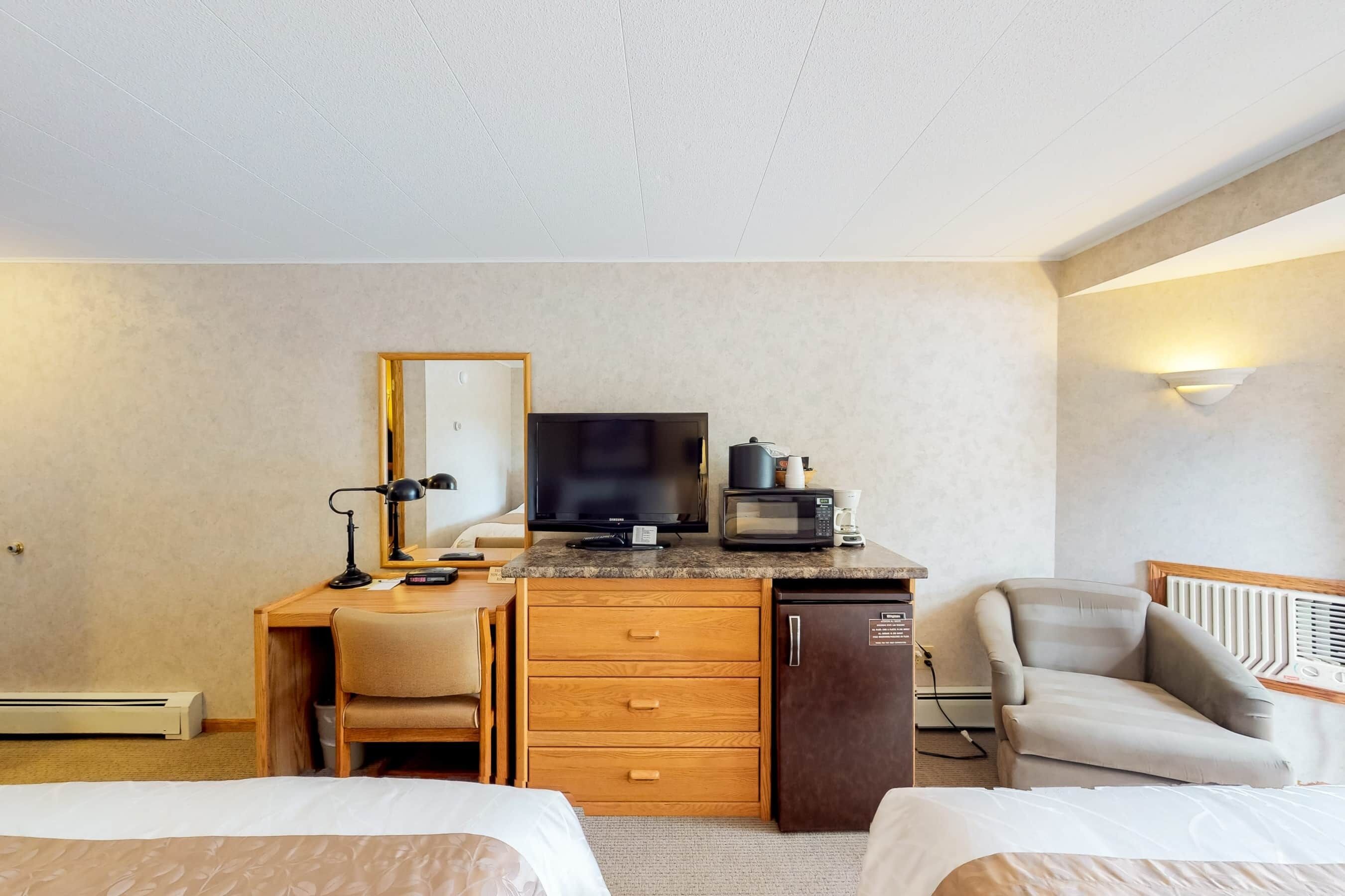 A hotel room with a wooden desk, a television, a microwave, a refrigerator, a chair, and two beds.