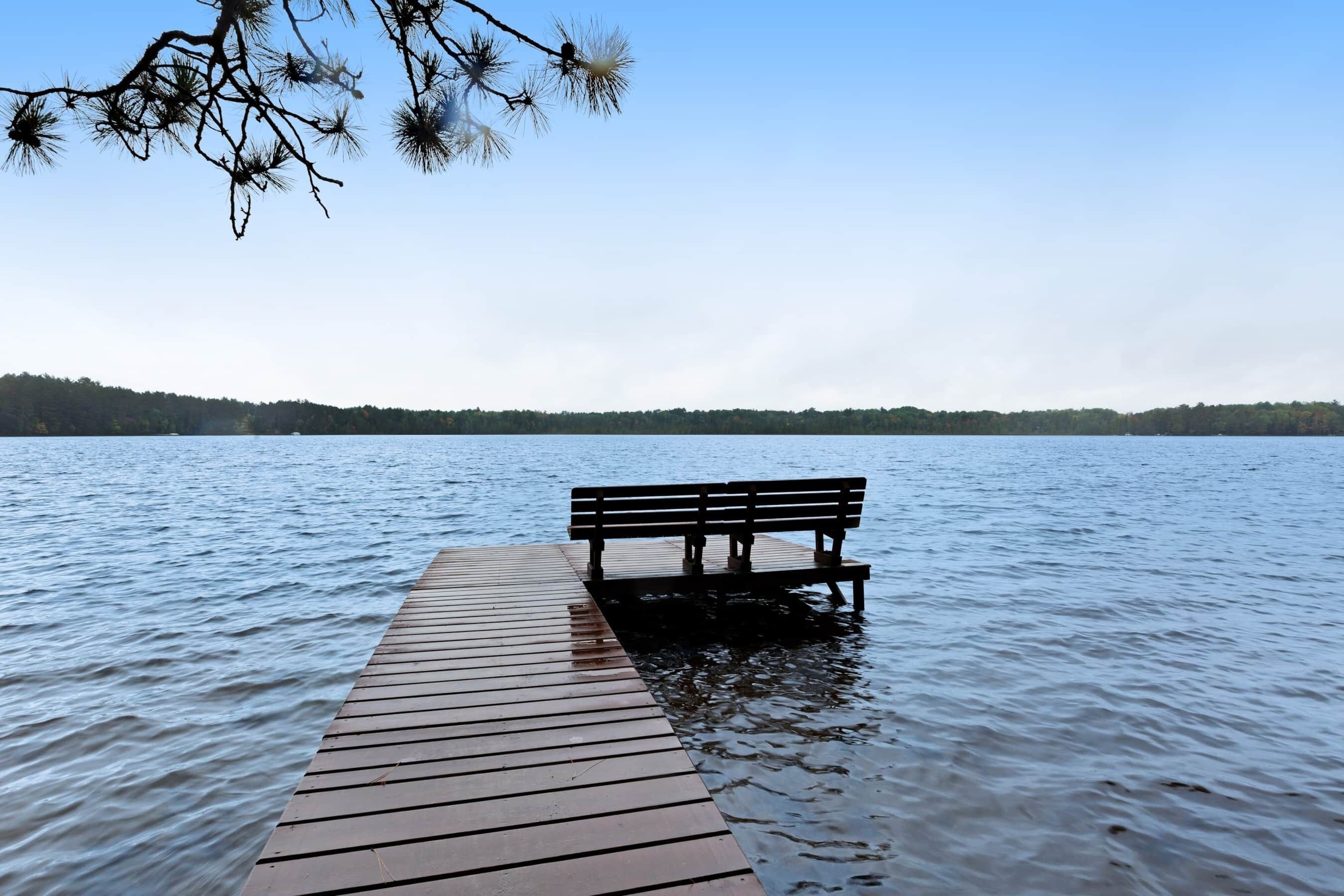 A wooden pier extending into calm water with a bench at the end.