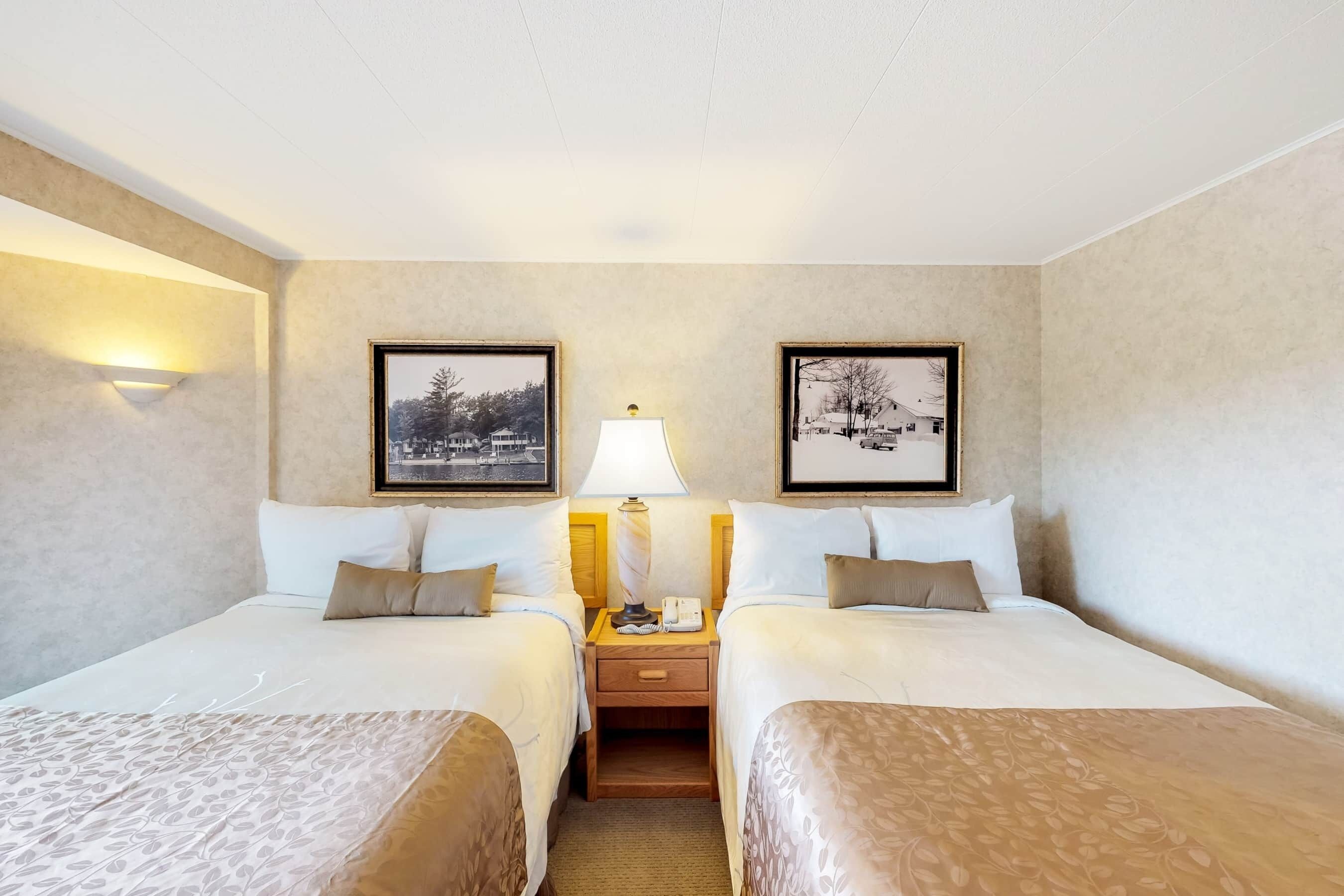 Une chambre d’hôtel avec deux lits, une table de chevet avec une lampe et des tableaux encadrés aux murs.