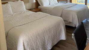 Et hotelværelse med to senge, en træsenggavl, et natbord med lampe og et stort vindue med udsigt til en bro og træer.