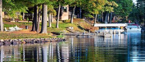 A lakeside view with a dock, trees, and a building with a covered area.