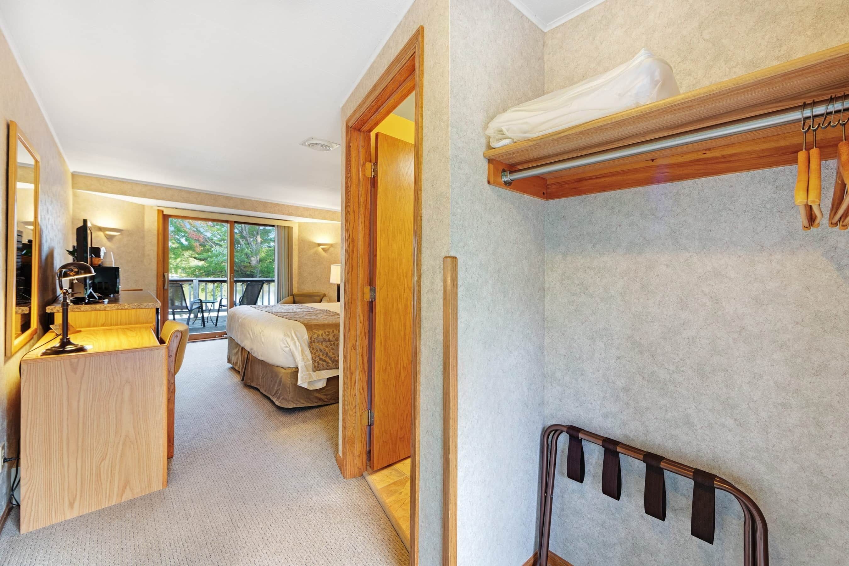 Ein Hotelzimmer mit Bett, Schreibtisch mit Lampe, Badezimmer mit Handtuchhalter und Blick ins Freie.