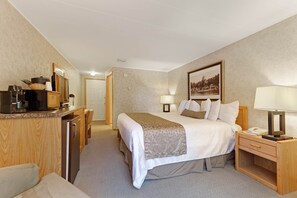 Hotellihuone, jossa on sänky, yöpöydät, työpöytä, jossa on kahvinkeitin, ja pieni jääkaappi.