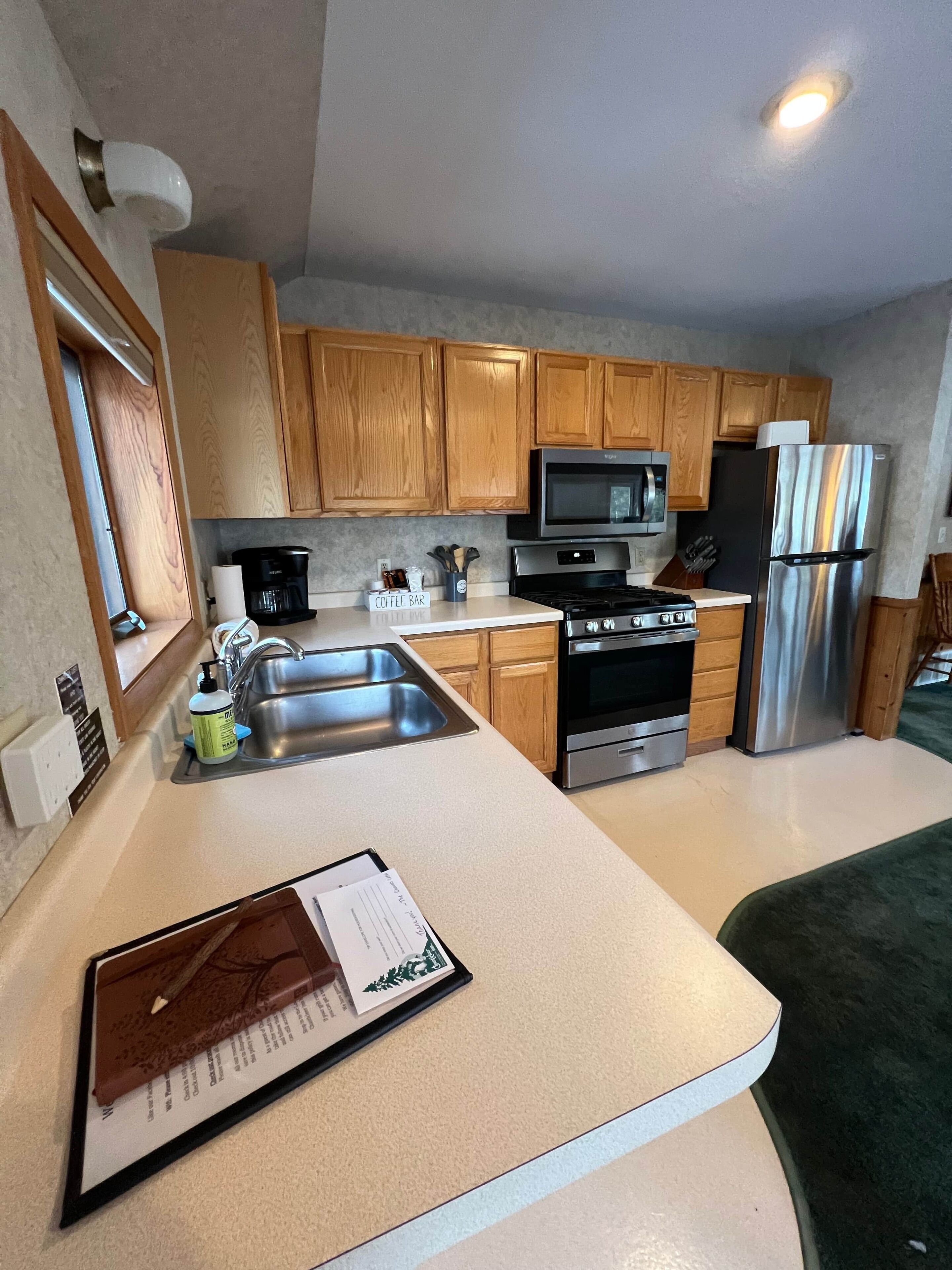 A modern kitchen with wooden cabinets, stainless steel appliances, and a countertop with a coffee maker and utensils.