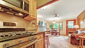 A kitchen with a stove, microwave, and wooden cabinets. There is a dining area with chairs and a table. - Chanticleer Inn Villa 4 (Eagle River)