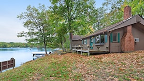 A lakeside cabin with a deck overlooking the water, surrounded by trees and a grassy area with fallen leaves. - Chanticleer Inn Villa 4 (Eagle River)