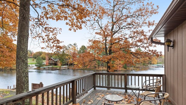 A wooden deck with chairs overlooking a lake, surrounded by trees with autumn leaves. - Chanticleer Inn Villa 5 (Eagle River)