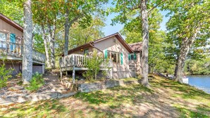 Une cabane dotée d’une terrasse, entourée d’arbres et bordée par un lac.