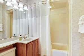 A bathroom with a white sink, wooden cabinets, a mirror, and a shower curtain. - Chanticleer Inn Villa 7 (Eagle River)