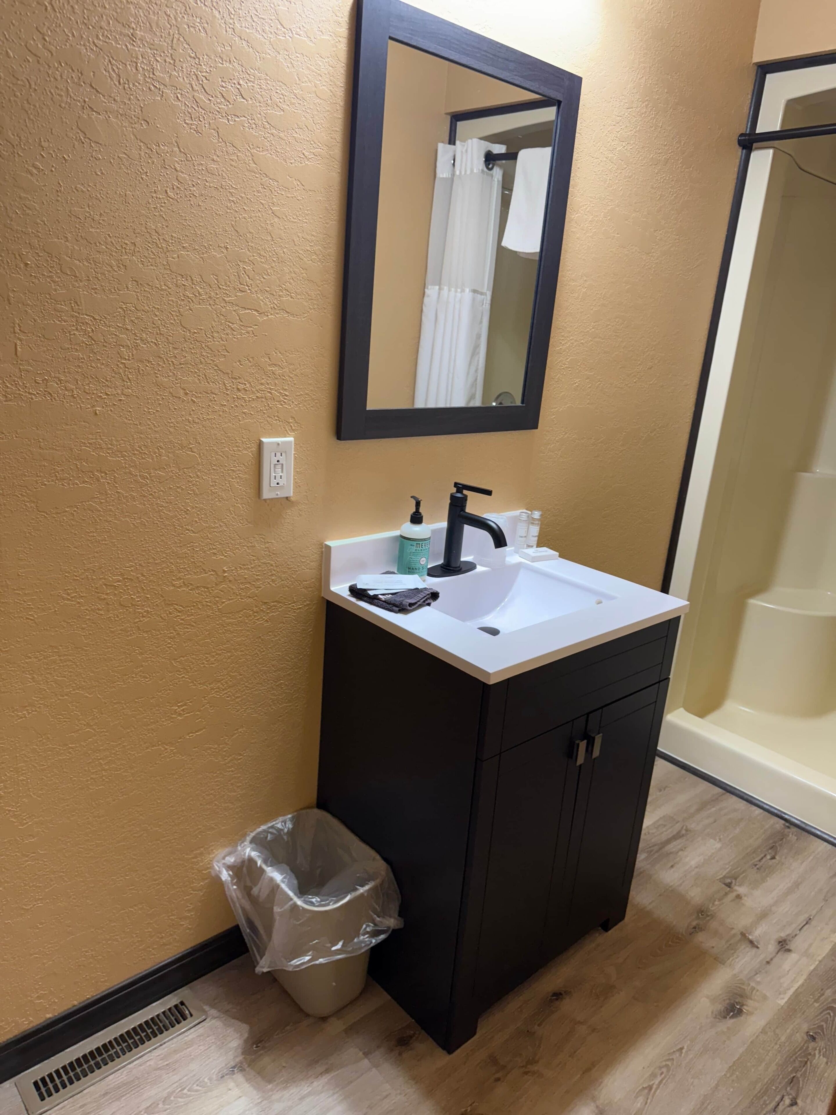 A bathroom with a white sink, dark cabinet, and a mirror above it.
