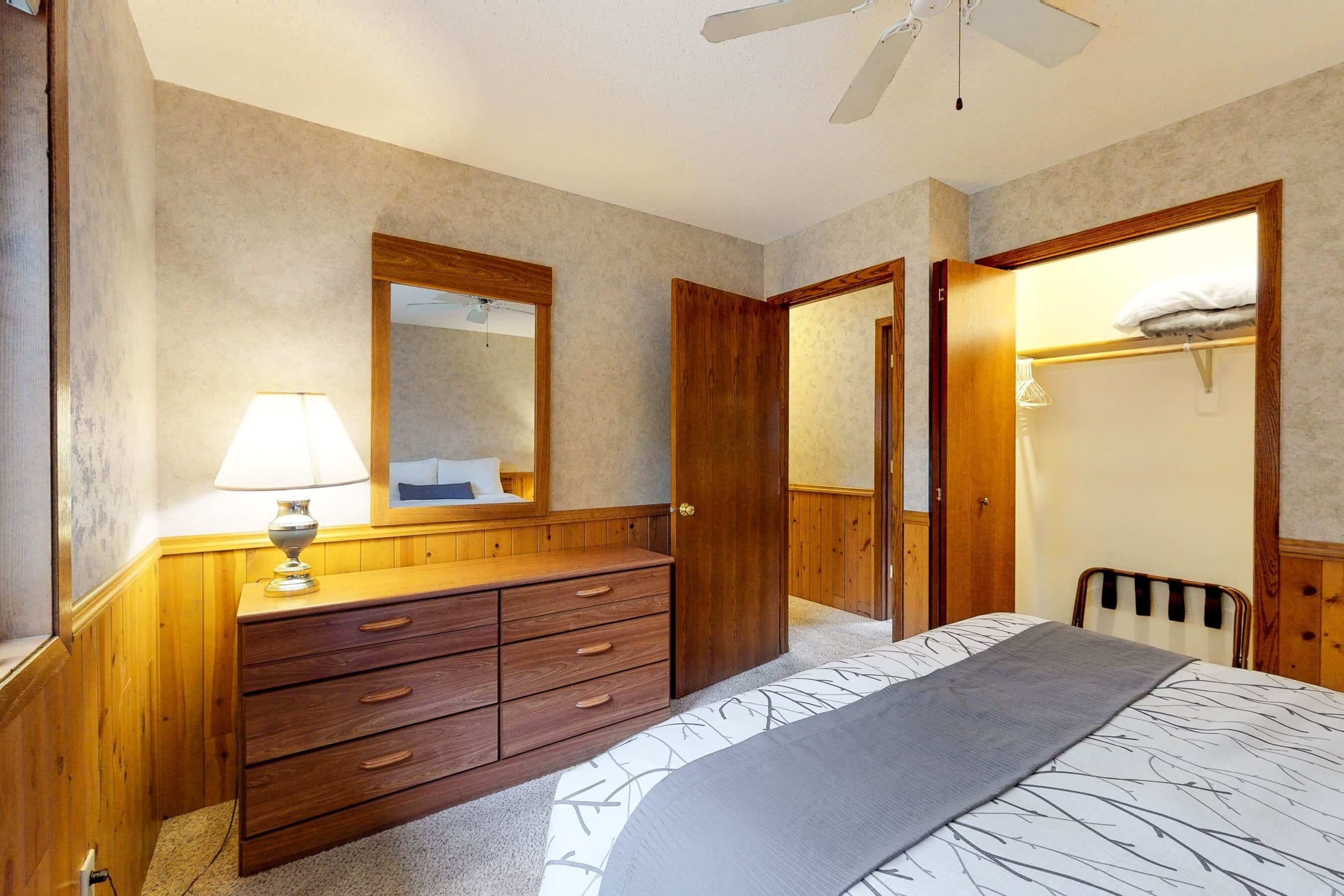 Een slaapkamer met een houten dressoir, een bed met een decoratieve spreidek en een plafondventilator.