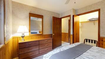 Een slaapkamer met een houten dressoir, een bed met een decoratieve spreidek en een plafondventilator.