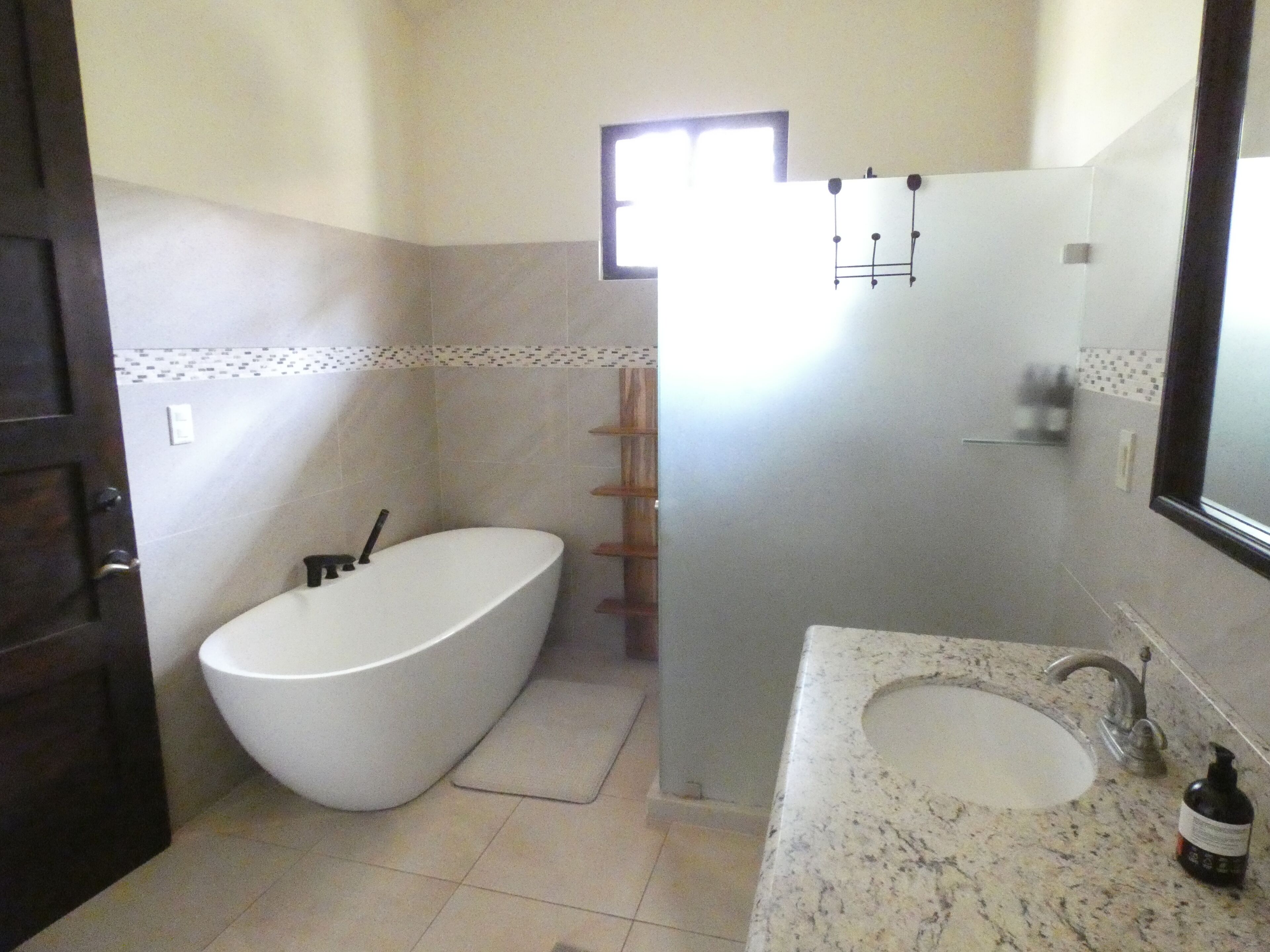 Une salle de bain dotée d’une baignoire îlot, d’un lavabo avec un plan de toilette en marbre et d’une fenêtre laissant entrer la lumière naturelle.