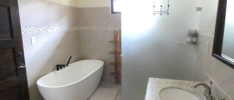 Une salle de bain dotée d’une baignoire îlot, d’un lavabo avec un plan de toilette en marbre et d’une fenêtre laissant entrer la lumière naturelle.