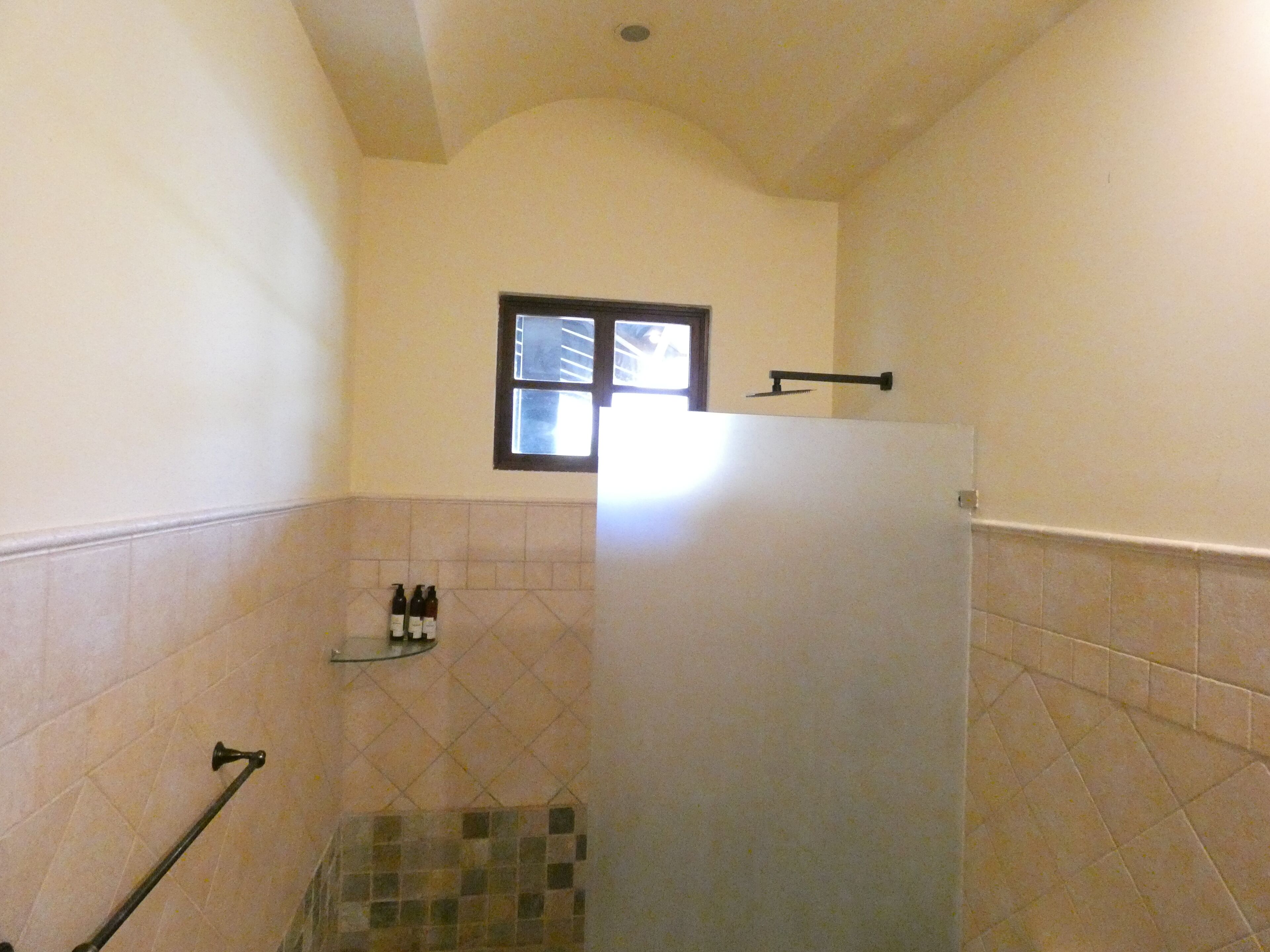 Un baño con ducha, paredes con azulejos, una ventana y un estante con artículos de aseo.