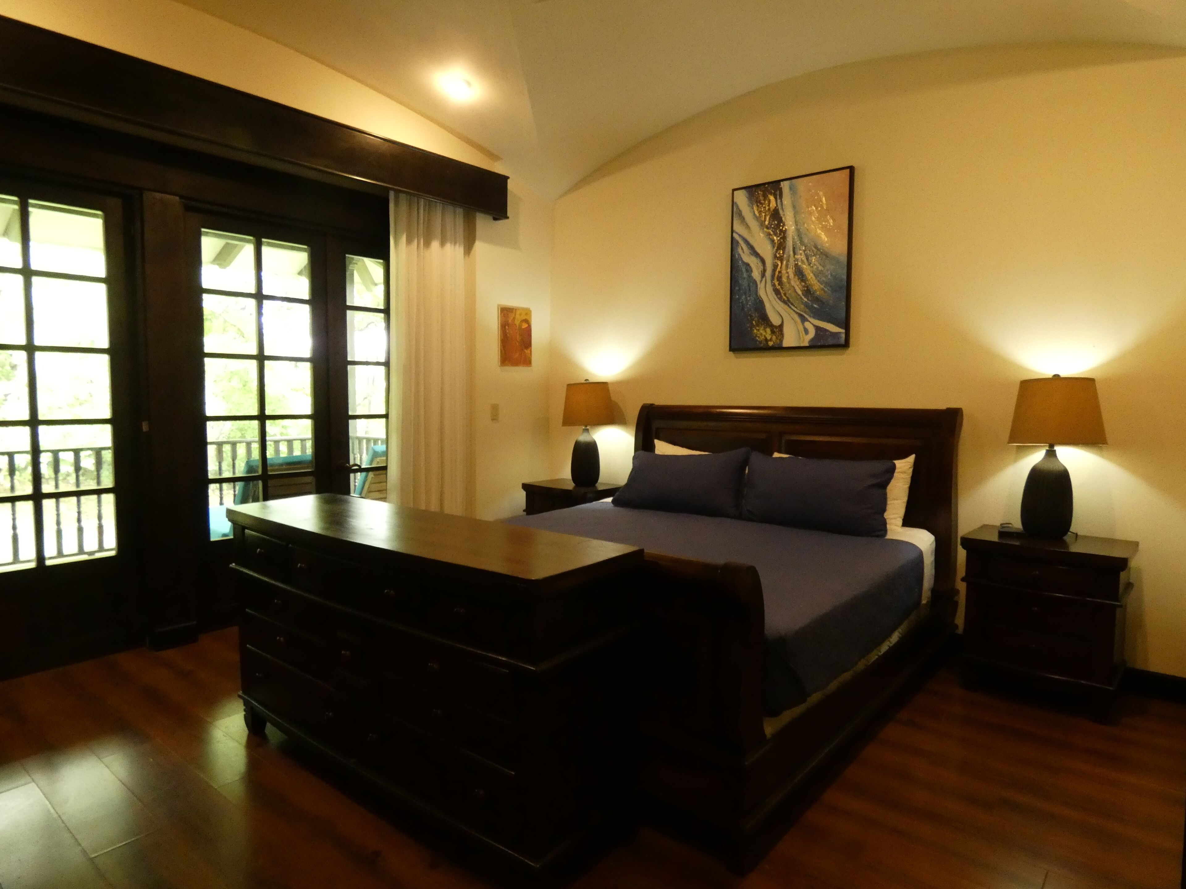 A bedroom with a bed, a dresser, a nightstand, and a painting on the wall.