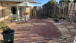 A patio area with a brick floor, a table with chairs, a green umbrella, and a wooden fence. - sweet little casita (Santa Fe)