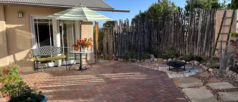 A patio area with a brick floor, a table with chairs, a green umbrella, and a wooden fence.