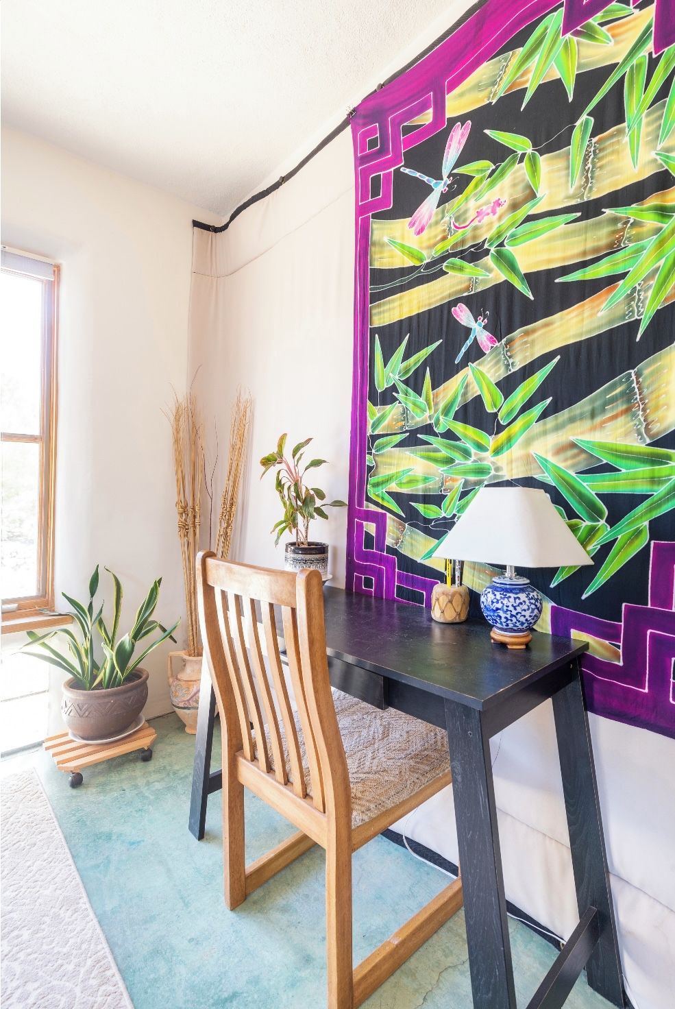 A corner room with a wooden chair, a small table with a lamp, and a wall with a bamboo leaf pattern.