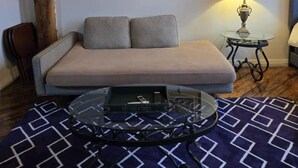Un salon avec un canapé, une table basse en verre, une lampe et un tableau au mur.