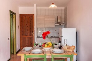 Un coin repas avec une table en bois dressée pour deux personnes, un panier de fruits et une bouteille de vin.