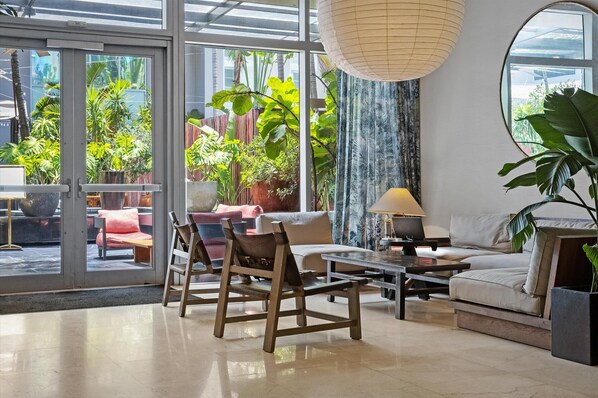 Uma sala de estar moderna com uma grande porta de vidro que dá para uma varanda com plantas, um sofá, cadeiras e uma mesa de centro.